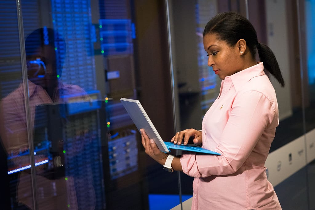 Seorang cloud engineer memantau infrastruktur server di data center menggunakan laptop.