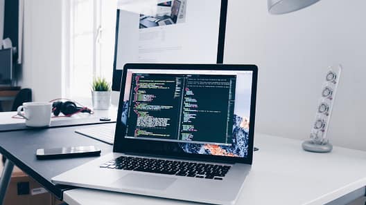 Laptop menampilkan kode pemrograman di atas meja kerja — belajar Python dari nol
