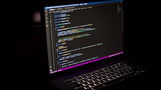 Laptop screen showing colorful JavaScript code in a dark environment, illustrating web development programming